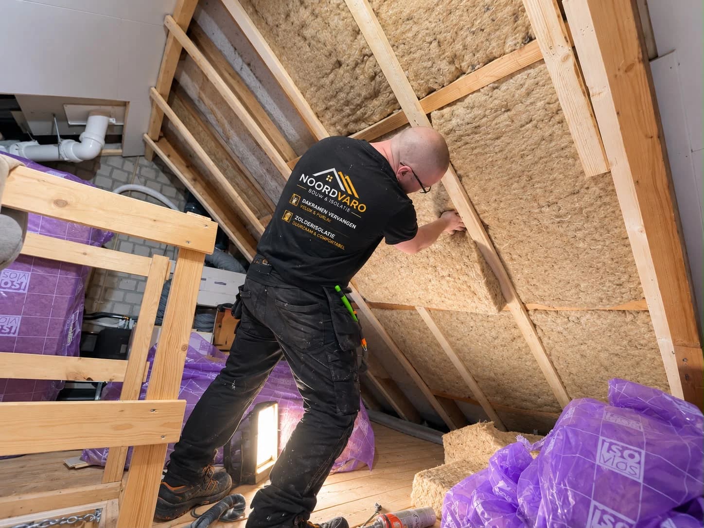 A Noordvaro specialist fits flax insulation between timber battens in an attic in Assen