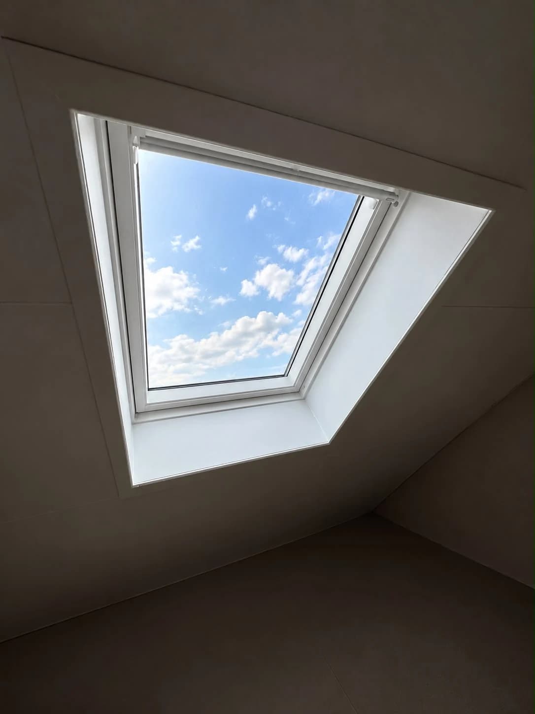 VELUX roof window with white interior lining, a top control bar and blue sky visible through the glass