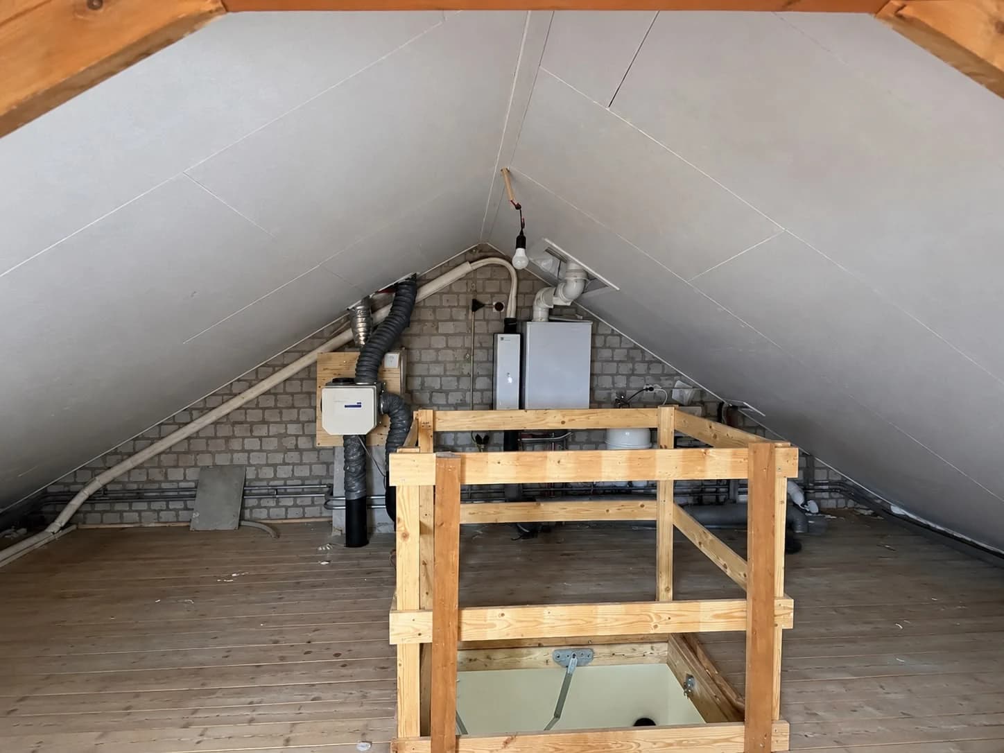 Attic with white sloping panels, a timber stair guard and services against the rear wall
