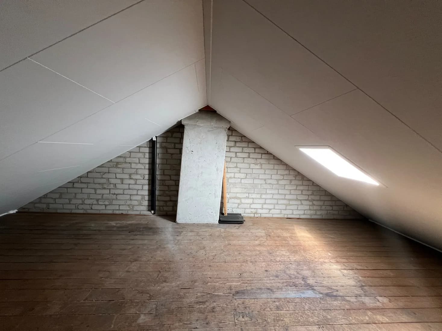 Zolderruimte met wit afgewerkte schuine wanden, een dakraam en houten vloer