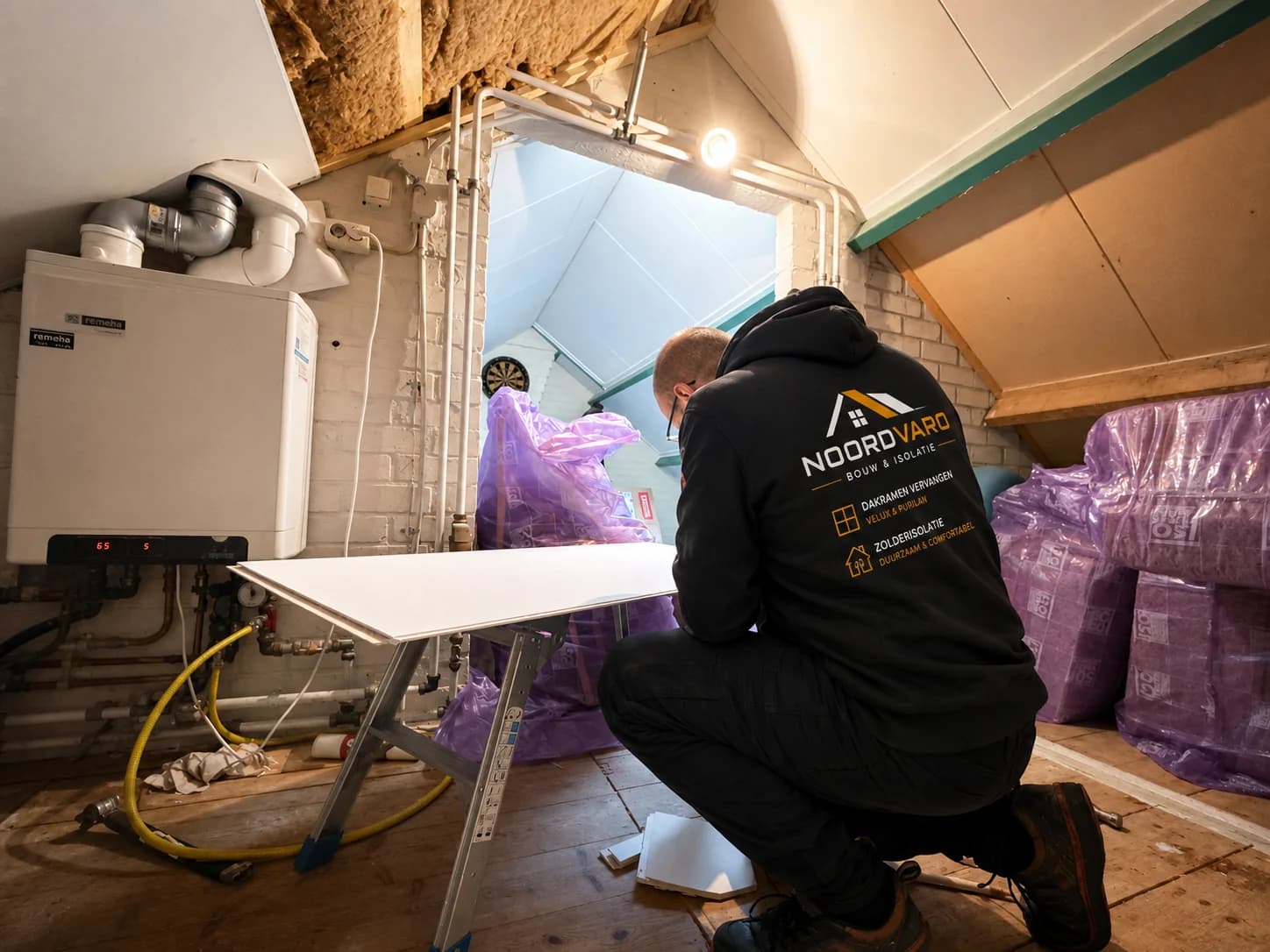 A Noordvaro installer prepares sheet material beside insulation supplies in an attic