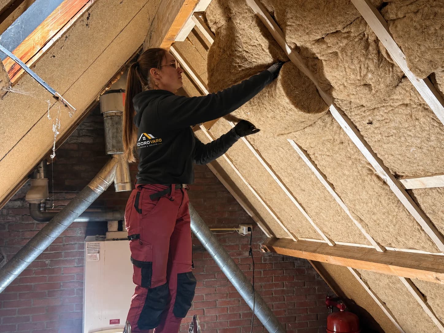 A Noordvaro team member fits stone wool between timber battens beneath a pitched roof